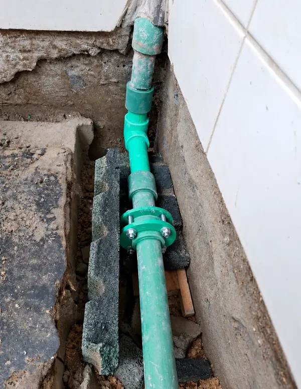 Tubo verde em vala junto a uma parede revestida.