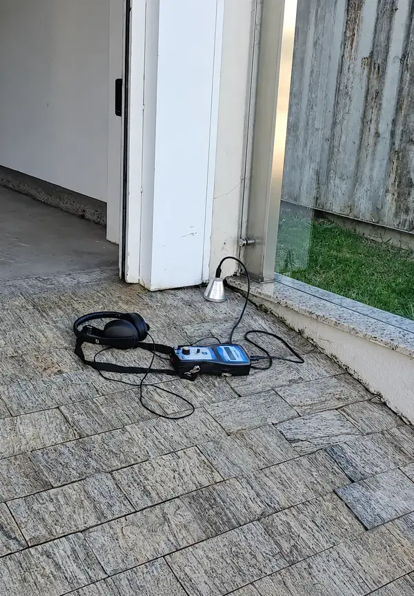 Pequeno aparelho eletrônico sobre piso pavimentado junto a uma porta.